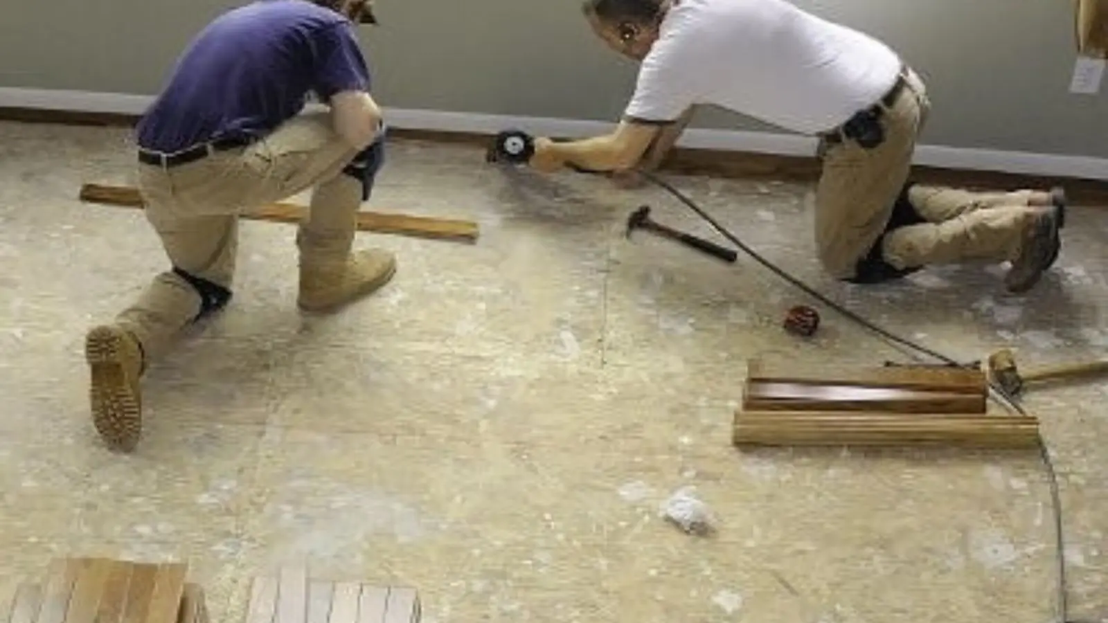 Two contractors kneeling on a stripped subfloor to rebuild a room after water damage